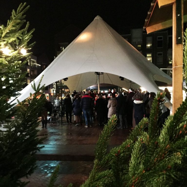 Kerstkoor onder starshade tent tijdens kerstmarkt in Hardenberg